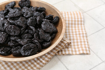 Wooden bowl with dried prunes on white tile background