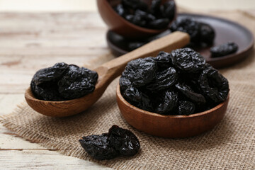 Bowl and spoon with dried prunes on white wooden background