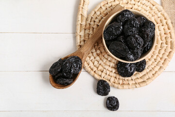 Bowl and spoon with dried prunes on white wooden background