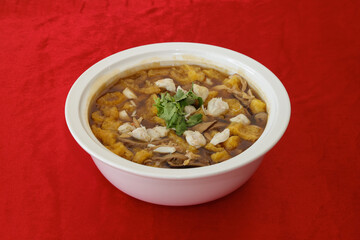A vibrant bowl of flavorful stew featuring meat, vegetables, and garnished with herbs, presented on a striking red background.