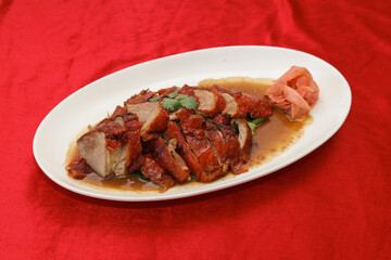 A beautifully plated dish featuring succulent roast meats in a savory sauce, garnished with herbs, served on a white platter against a vibrant red background.