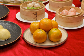 A vibrant display of Chinese dim sum, featuring a plate of oranges, bamboo steamers, and a red tablecloth, creating an inviting culinary atmosphere.