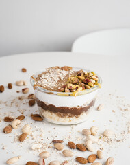 A delicious layered dessert featuring a creamy mixture topped with pistachios, almonds, and cashews, set in a clear glass container. The dessert is beautifully arranged with layers of white chocolate