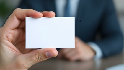 A hand holding a blank white card, close-up focus, with a blurred professional background, creating a clean and minimalistic look.