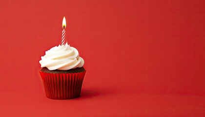 A beautifully decorated chocolate cupcake with a lit candle on top against a vibrant red background