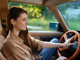 Fototapeta premium Smiling young woman driving a vintage car, wearing casual clothing, with a vibrant green background, evoking a sense of freedom and adventure.