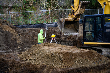 New home construction foundation earthwork, surveyor with laser level range finder, heavy equipment...
