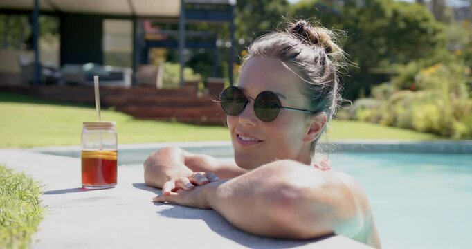 Relaxing in pool, woman smiling with sunglasses and iced tea on sunny day