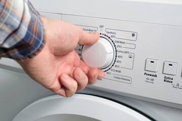 A man's hand sets the washing mode temperature switch on the washing machine.