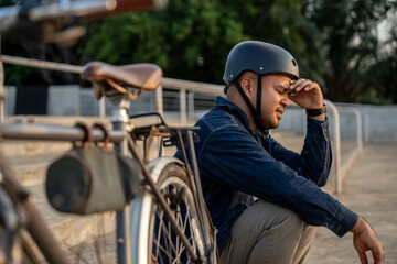 Stressed asian tourist man sitting near bicycle in the urban city background