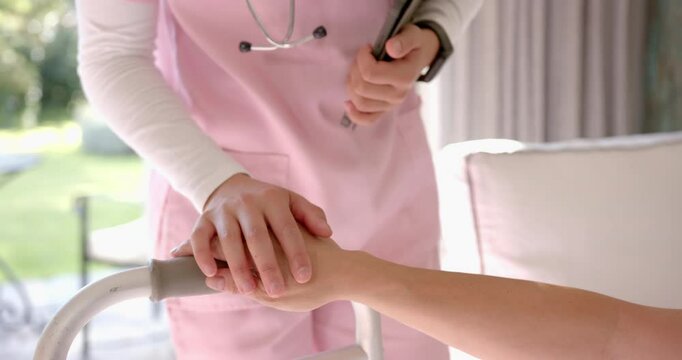 Nurse in pink scrubs holding clipboard, assisting patient with walker