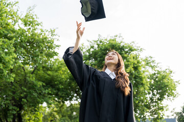Happy asian woman in graduation costume with cap standing outdoor public park. College degree...