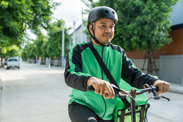 Obraz premium Portrait Rider food delivery man wearing green uniform and helmet cycling a bicycle the food service to customer. Happy delivery man with green backpack shipping of goods to customers.