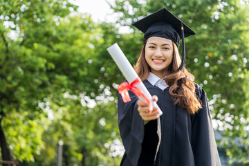 Happy asian woman in graduation costume with cap standing outdoor public park. College degree...