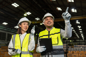 Professional engineer and technician wearing safety helmet analyzing meeting with tablet in factory warehouse. Confident factory workers group inspection industry factory. Teamwork concept.