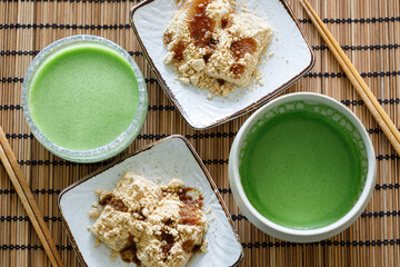 Cup of fresh matcha tea and Warabi mochi, traditional Japanese sweet from bracken starch on wooden table.