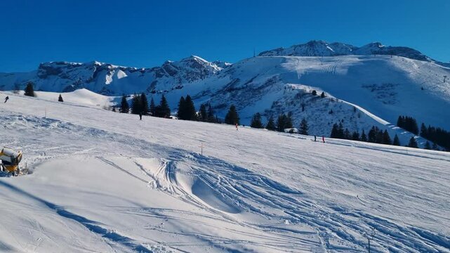 Skiers glide down a snowy slope, filmed from a moving ski lift. The iconic Wildstrubel peak stands in the backdrop of the Bernese Alps, captured on a sunny day at B&uuml;hlberg in Adelboden Lenk