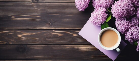 Top view of a rustic wooden table featuring lilac flowers, a purple notebook, and a coffee cup on the right, with ample copy space on the left