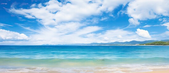 Fototapeta premium Tranquil seascape of Miyakojima Okinawa featuring a clear blue ocean blending into a vibrant sky with fluffy white clouds and ample sandy shore space