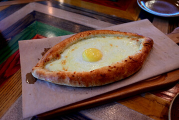 Freshly baked khachapuri served on a wooden board with a cracked egg yolk on top at a vibrant eatery