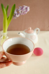 Hand holding a teacup with easter eggs in the background.







