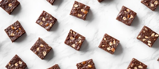 Richly textured brownies with nuts arranged in a grid pattern on a white marble background showcasing their enticing presentation and cocoa flavor.
