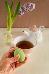 hand holding green easter egg with spring tea setup