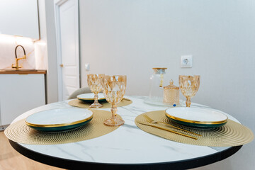 In a warm kitchen, a round dining table is elegantly set with beautiful plates and sparkling wine glasses, creating an ideal space for family gatherings and joyful celebrations