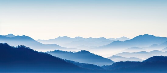 Fototapeta premium Serene mountain range with layered silhouettes in bluish tones and soft morning fog creating a tranquil atmosphere across the landscape