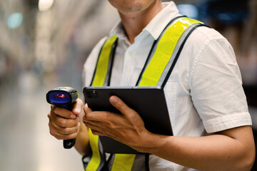 A man wearing a safety vest is holding a tablet and a barcode scanner. He is likely working in a warehouse or a similar environment where he needs to scan items for inventory or tracking purposes