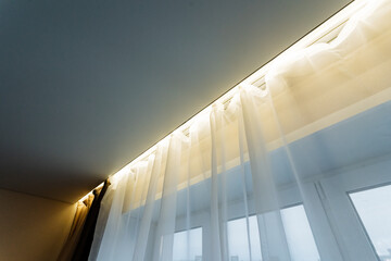 A white curtain gracefully hangs down from the ceiling, elegantly positioned next to a window,...