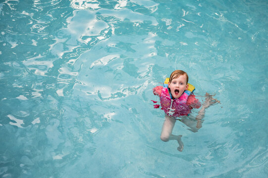 Young girl in a life jacket swimming in a clear blue pool.