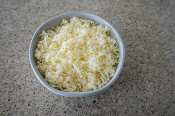 Ceramic white bowl full of shredded white cheese, speckled countertop.