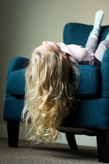 Playful young girl smiling upside down on a chair