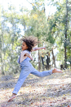 A carefree child in overalls leaps gracefully in a sunny forest.