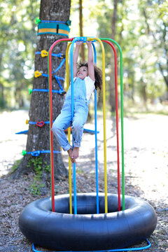 A child in overalls hangs on colorful playground bars over a tir