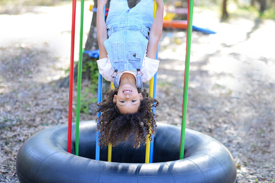 A cheerful child in overalls hangs upside down on colorful playg