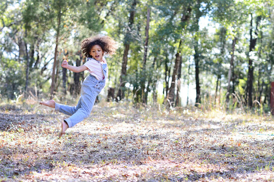 A cheerful child in overalls leaps energetically in a forested