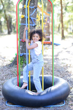 A smiling child in overalls climbs colorful playground bars on a