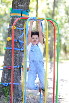 Smiling child in overalls hangs from colorful playground bars o