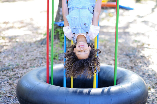 A laughing child in overalls hangs upside down on colorful bars.