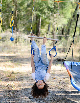 A smiling child in overalls hangs upside down on playground rope