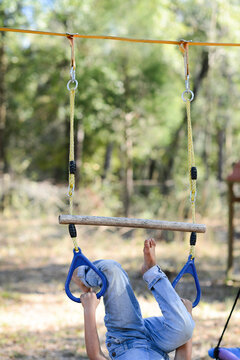 A child in jeans plays on a hanging rope swing set in a forested