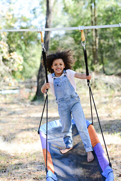 A smiling child in overalls stands on a colorful hammock swing o