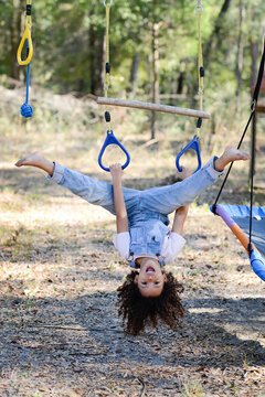 A playful child in overalls hangs upside down on a rope swing ou