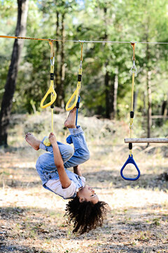 A child in overalls hangs upside down on yellow playground ropes