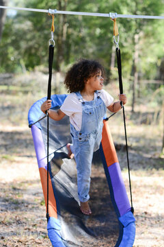 A child in overalls balances on a colorful hammock swing outdoor