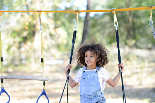 A child in overalls holds onto ropes on a playground swing outdo