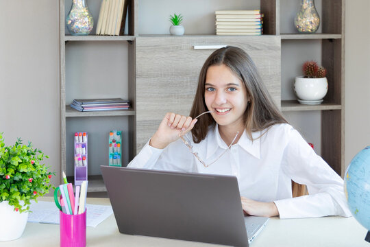 Smiling young teenage girl studying with laptop at table. - Powered by Adobe