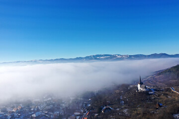 Aerial view of foggy misty mountain village and church tower at winter